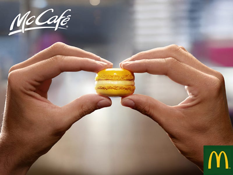 An advertisement for McCafe featuring two hands holding a macaron made to look like a tiny hamburger.